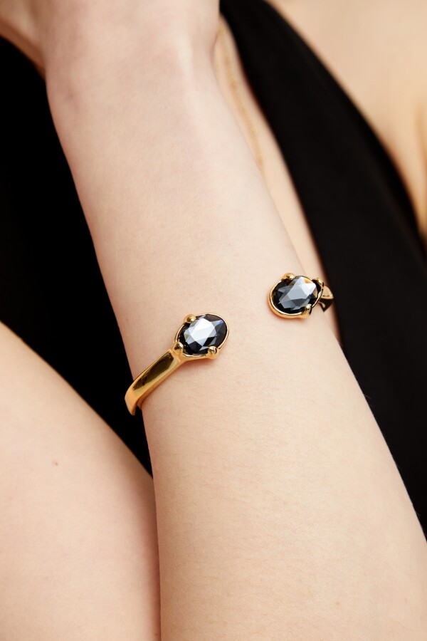 PULSERA RIGIDA DE ALEACIÓN DE METALES BAÑADA EN ORO 18K Y DOS CRISTALES FACETADOS GRISES EN EXTREMOS Pulsera